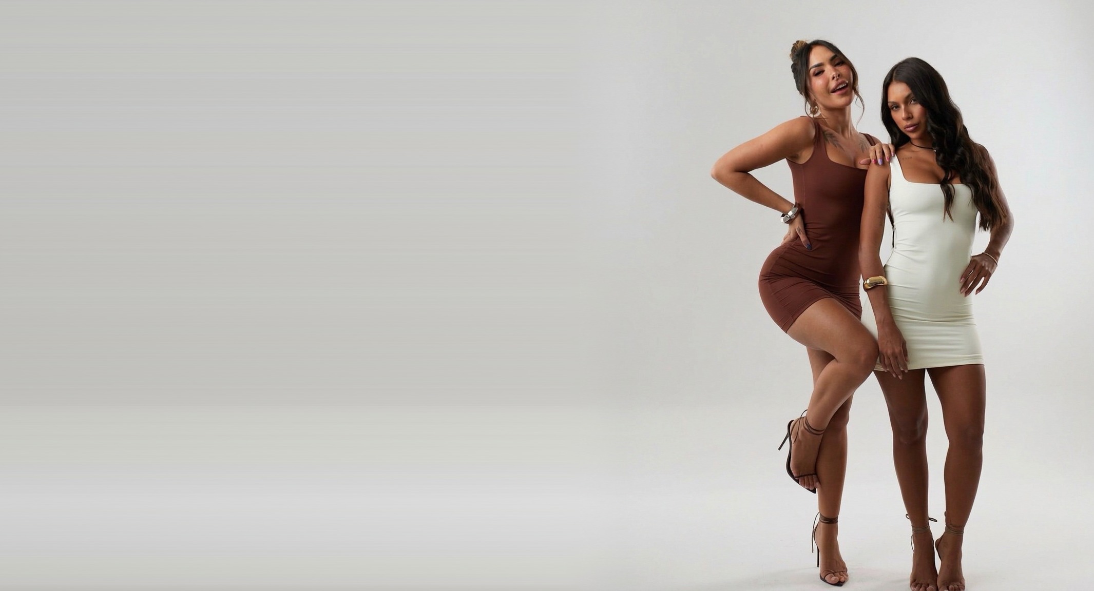 Duas modelos vestindo conjuntos justos, uma marrom e outra creme